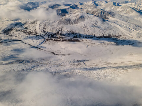 Aerial view of Babusar Pass featuring snow-covered mountain peaks and a winding road under soft clouds in Babusar, KPK, Pakistan.
