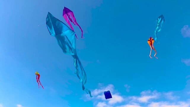 Many different colorful kites are flying in the blue sky and swaying in the wind during summer outdoor festival. Childhood, freedom and leisure time concept