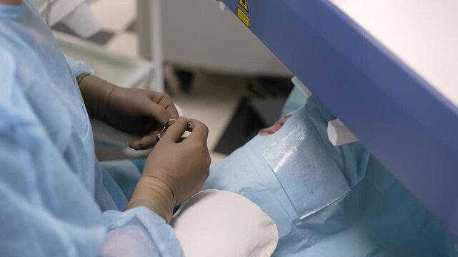 Close up of surgeon's hands in gloves performing ophthalmic surgery. Doctor uses medical instrument on patient's eye under a laser machine. Modern clinic and advanced technology in medicine