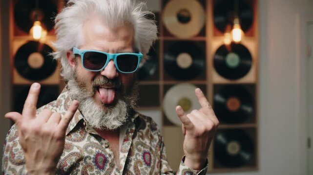 Mature man with white beard wearing light blue sunglasses gesturing rock and roll sign indoors