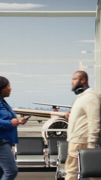 Vertical video Commuting, airport and tourists in transport hub waiting area overlooked by runway control tower. Walking, chair seats rows and people inside bright modern flight departure terminal