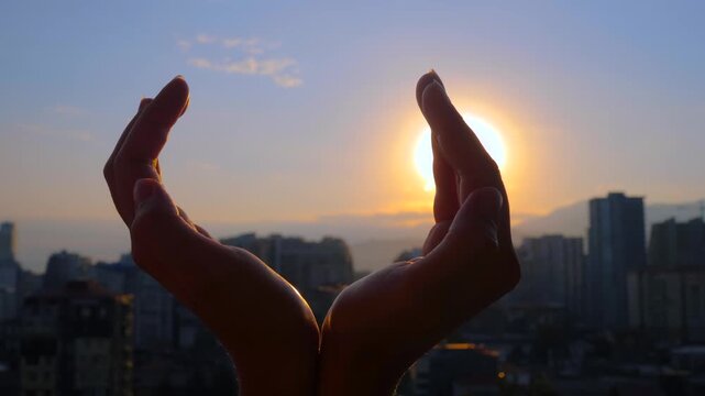 Silhouette of woman is holding sun between her hands at sunset or sunrise - close up view, sun lens flare. Relaxation, meditation, freedom and harmony concept