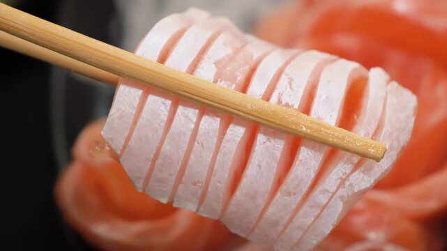 A cinematic close-up shot showing wooden chopsticks gently lifting a thick, fresh slice of raw salmon sashimi from a beautifully arranged platter. The footage highlights the vibrant orange color and d