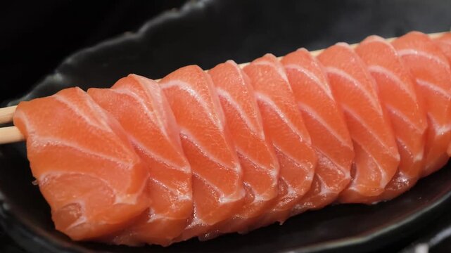 A close-up shot showcasing the rich texture and vibrant orange marbling of fresh, raw salmon sashimi slices. The pieces are neatly arranged in a traditional Japanese presentation on a dark ceramic pla