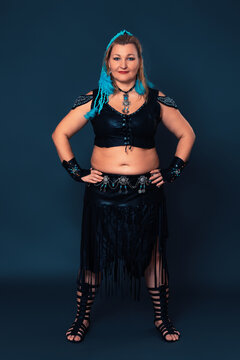 Mature female dancer is outfitted in professional grade performance costume, crafted by hand - leather top and skirt, along with bracers and gladiator boots, all of which are of highest quality design