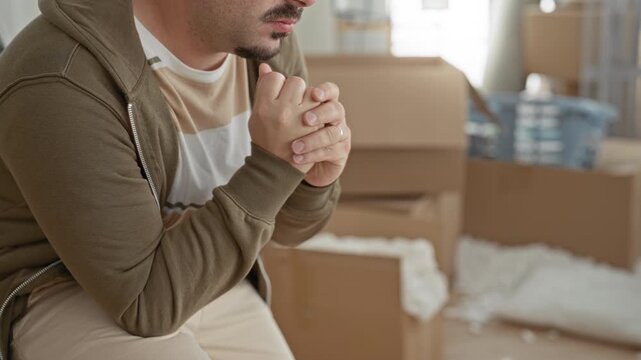 Man hands clasped near chin, leaning forward among cardboard boxes in a building during a move; transition anxiety.