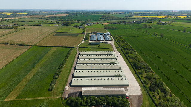 Aerial view of large industrial farm buildings and long agricultural sheds surrounded by vast green fields and rural landscape in Kettering, England, United Kingdom.