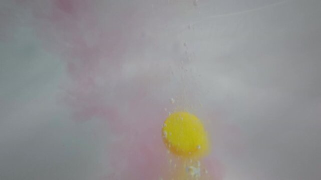 Underwater POV shows yellow bath bomb plunging into bathwater