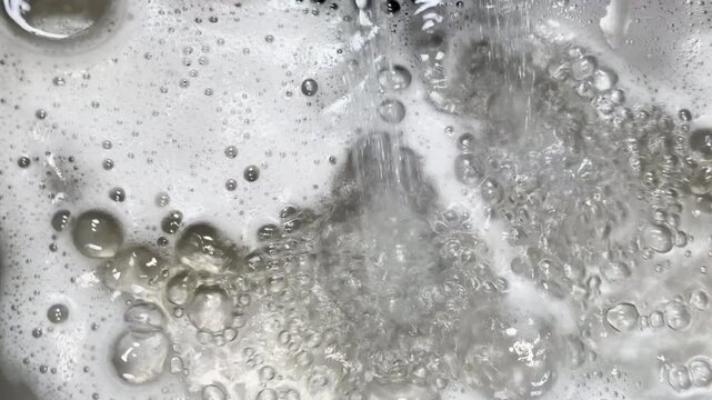 Water pouring into sink creates background plate of soapy bubbles