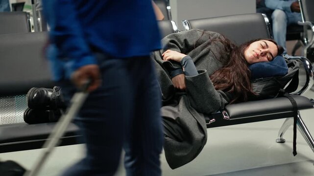 Tired woman in airport lounge sleeping on metal bench during long airplane layover. Jet lagged traveler resting on seats, napping on neck pillow while waiting for delayed plane, camera A