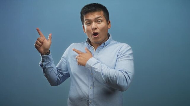 Man in light blue shirt points finger to left with finger gun gesture in studio; playful confidence.