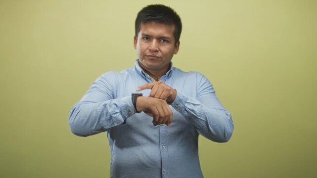 Man points finger to wristwatch in studio while checking time with closed eyes and a focused expression; impatience punctuality timekeeping.
