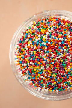 A top down view of a condiment cup full of nonpareils rainbow sprinkles.