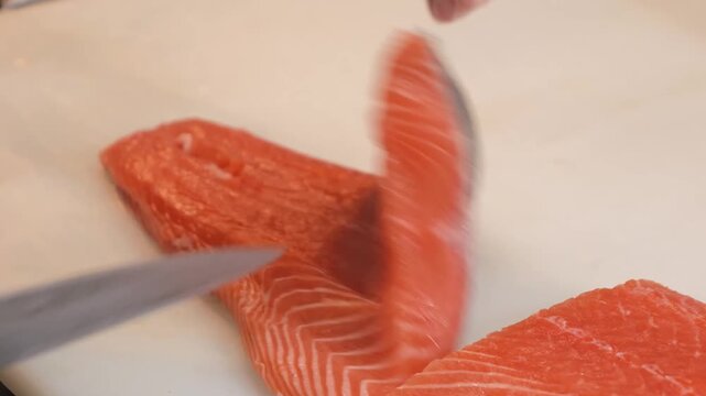 A detailed close-up shot showing the process of filleting a fresh, vibrant red salmon. The footage captures the precise technique of slicing the raw fish on a professional cutting board, highlighting 