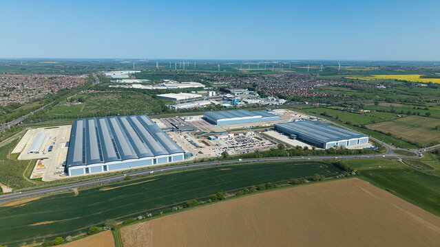 Aerial view of Symmetry Park industrial estate featuring large modern warehouses and parking facilities surrounded by green fields in Kettering, England, United Kingdom.