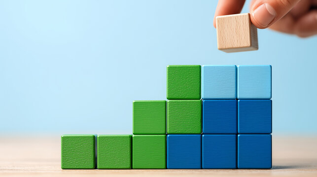 Ascending Blocks of Growth: A hand delicately places a wooden block atop a vibrant structure of colorful blocks, illustrating the concept of growth, progress, and development. 