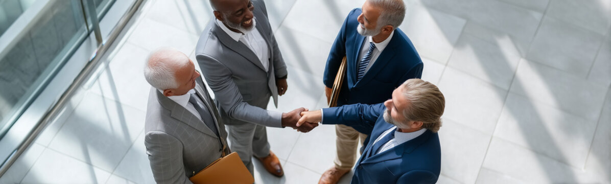 Business Handshake: An elevated perspective captures a moment of agreement as two business associates clasp hands in a decisive handshake, while two colleagues look on.