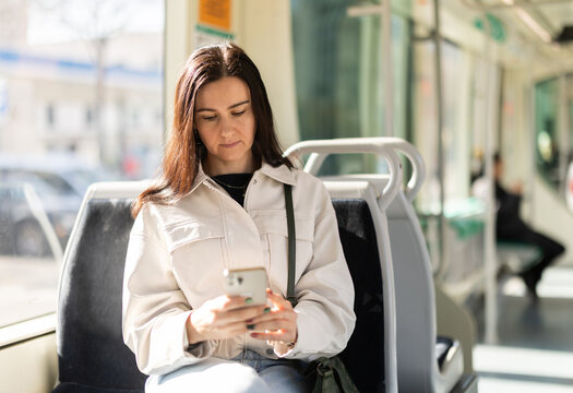 Girl sitting in modern tramway car. Passenger scrolls through social media feed, reads news online. Bored passenger whiles away time on social media