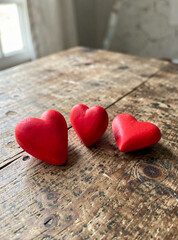 Fototapeta premium The image shows three red hearts resting on a wooden surface with visible grain and texture. The background is indistinct but appears to be an interior space.