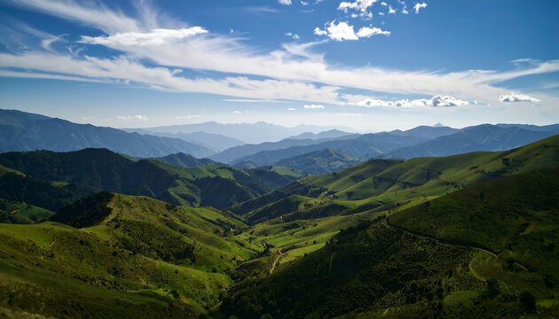 Verdant hills roll towards distant mountain ranges under a bright blue sky with fluffy white clouds, offering a scenic vista