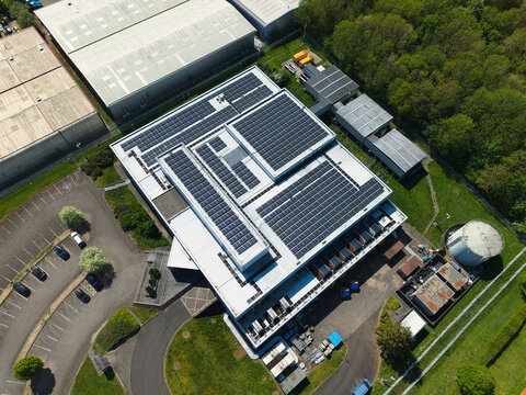 Aerial view of a modern data centre with extensive rooftop solar panels and adjacent parking facilities in Wellingborough, England, United Kingdom.