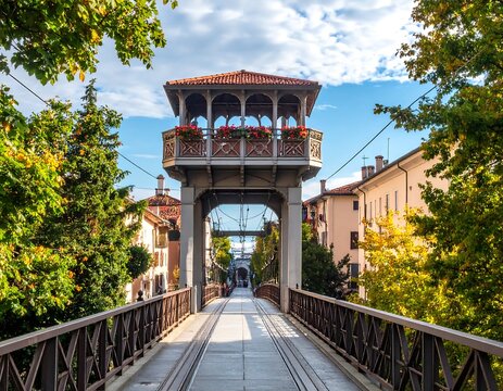 View of an ornate bridge with a detailed pavilion and walkways. Trees and buildings flank the scene, beneath a blue sky