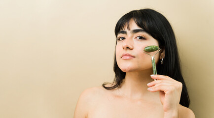 Latin woman using a jade roller on her cheek, taking care of her skin during a beauty routine © AntonioDiaz