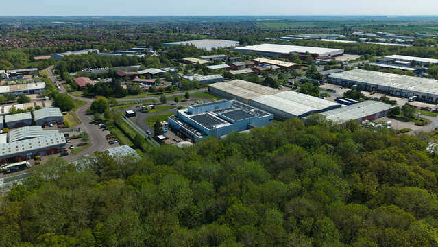 Aerial view of a modern data centre with solar panels on the roof surrounded by lush green trees and industrial warehouses in Wellingborough, England, United Kingdom.