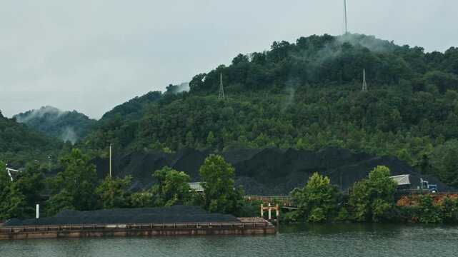 Barge full of coal traveling down a river near a depot on a misty Appalachian mountain morning