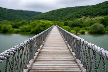Fototapeta premium Scenic wooden suspension bridge over river in lush green landscape