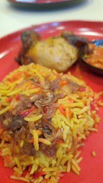 Close-up of authentic Arabian Chicken Mandi rice served on a vibrant red plate in a Middle Eastern restaurant. The footage features fragrant basmati rice, roasted chicken, fresh cucumber slices,sambal