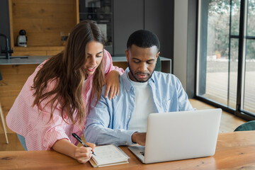 A couple collaborates at their kitchen table, using a laptop and notebook to plan finances, schedule tasks and projects while sharing ideas and staying focused in a bright modern home setting. © Daniel