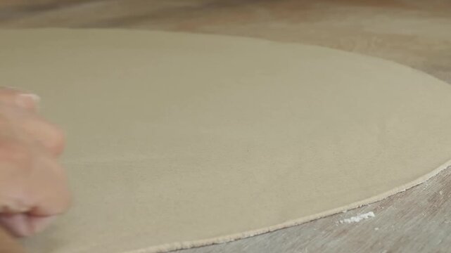 close-up shot capturing the process of hand-rolling a large, circular clay slab on a wooden workbench. The footage highlights the smooth texture of the pliable clay and the steady motion of a wooden r