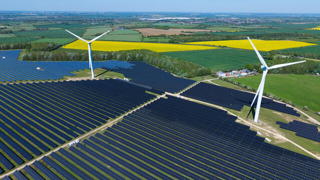 Aerial view of Chelveston Wind Farm featuring solar panels and wind turbines surrounded by green and yellow fields in Wellingborough, England, United Kingdom.
