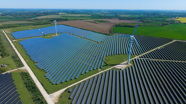Aerial view of Chelveston Wind Farm featuring vast solar panel arrays and wind turbines across the green countryside in Wellingborough, England, United Kingdom.
