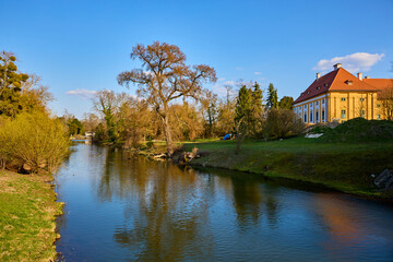 Fototapeta premium Tranquil river landscape with historic building and blue sky in spring