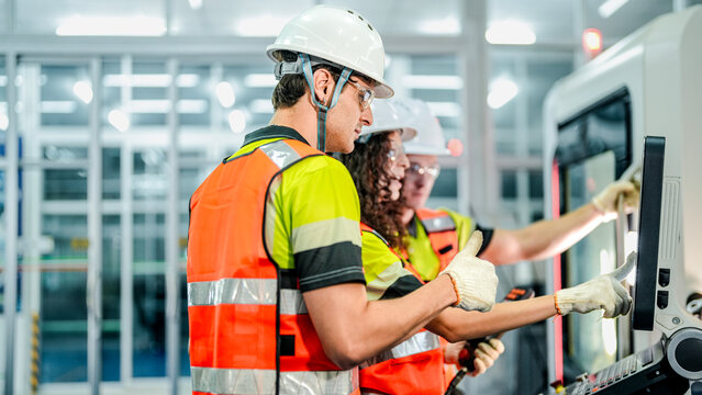 Three engineers program an industrial robot or CNC machine using an AI interface. The team manufactures advanced microchips or high-tech components in a smart factory.