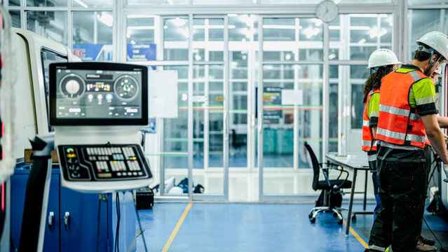 Three engineers program an industrial robot or 5-axis CNC machine using an AI interface. The team manufactures advanced microchips or high-tech components in a smart factory.