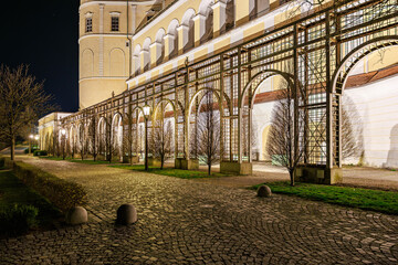 Fototapeta premium Illuminated architectural colonnade at night with trees and arched windows