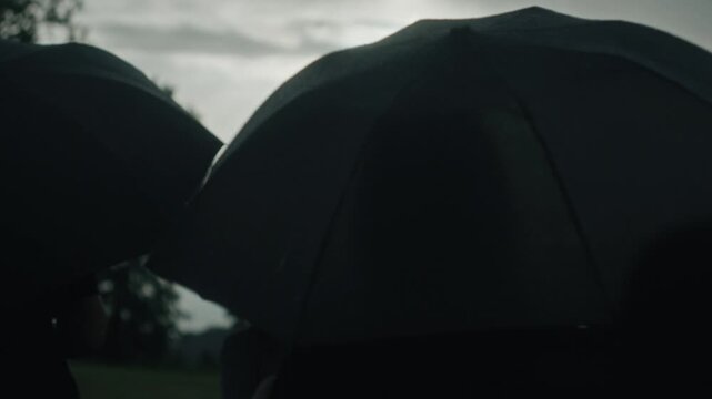 Silhouetted crowd of people walking under umbrellas on a cloudy day during a funeral procession