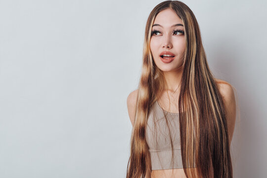 Young woman with long braided hair wearing a sleeveless top standing against a light background looking sideways with a thoughtful expression. Beauty and fashion concept.