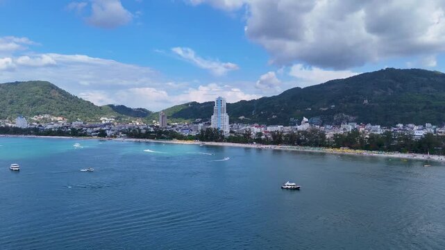 Scenic drone footage of patong beach thailand coastline with boats and cityscape.