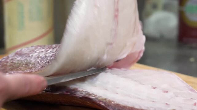 A detailed close-up footage of a professional chef's hands using a sharp knife to fillet a fresh red snapper fish. The video captures the precise technique of separating the delicate white flesh from 