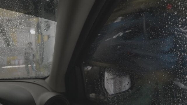 Auto detailing and maintenance concept: Interior car view looking through a wet passenger window as automated spinning brushes clean the exterior at a commercial car wash.