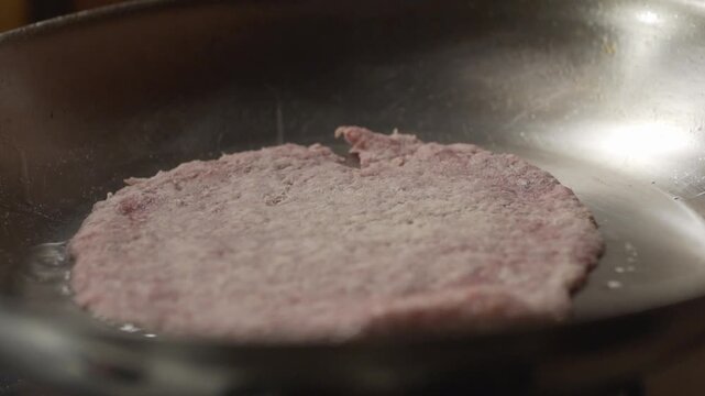 A breaded and raw schnitzel is cooked in a metal pan. Meanwhile, the oil bubbles as it keeps heating up.