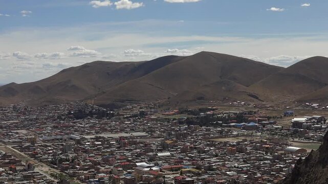 The city of Oruro, Bolivia, by day, filmed in a timelapse where clouds move quickly over the mountains and cast their shadows upon them.