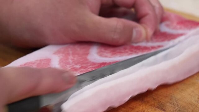 A detailed shot showing a hand inspecting or preparing a fresh slice of premium raw beef, characterized by intense white intramuscular fat (marbling). This high-quality meat, likely A5 Wagyu or Karubi