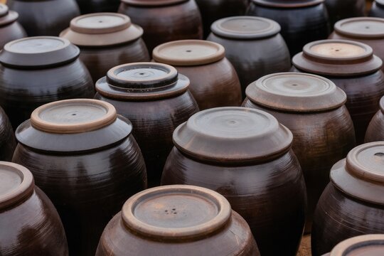 Traditional Korean onggi pots made of clay for food fermentation. Old brown ceramic jars with lids are stored outside a rustic house. Vintage pottery for kimchi and gochujang.