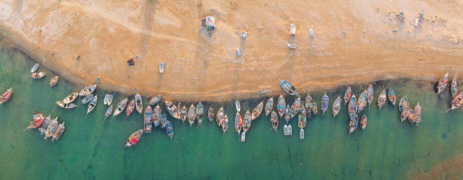 Aerial view of numerous colorful fishing boats moored along the sandy shoreline of the turquoise sea Gwadar, Balochistan, Pakistan.