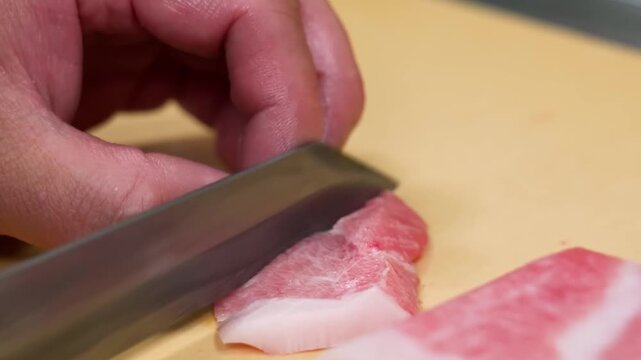 close-up, high-angle shot capturing a professional sushi chef's hands using a traditional Japanese yanagiba knife to expertly slice a piece of marbled fatty bluefin tuna (Otoro).